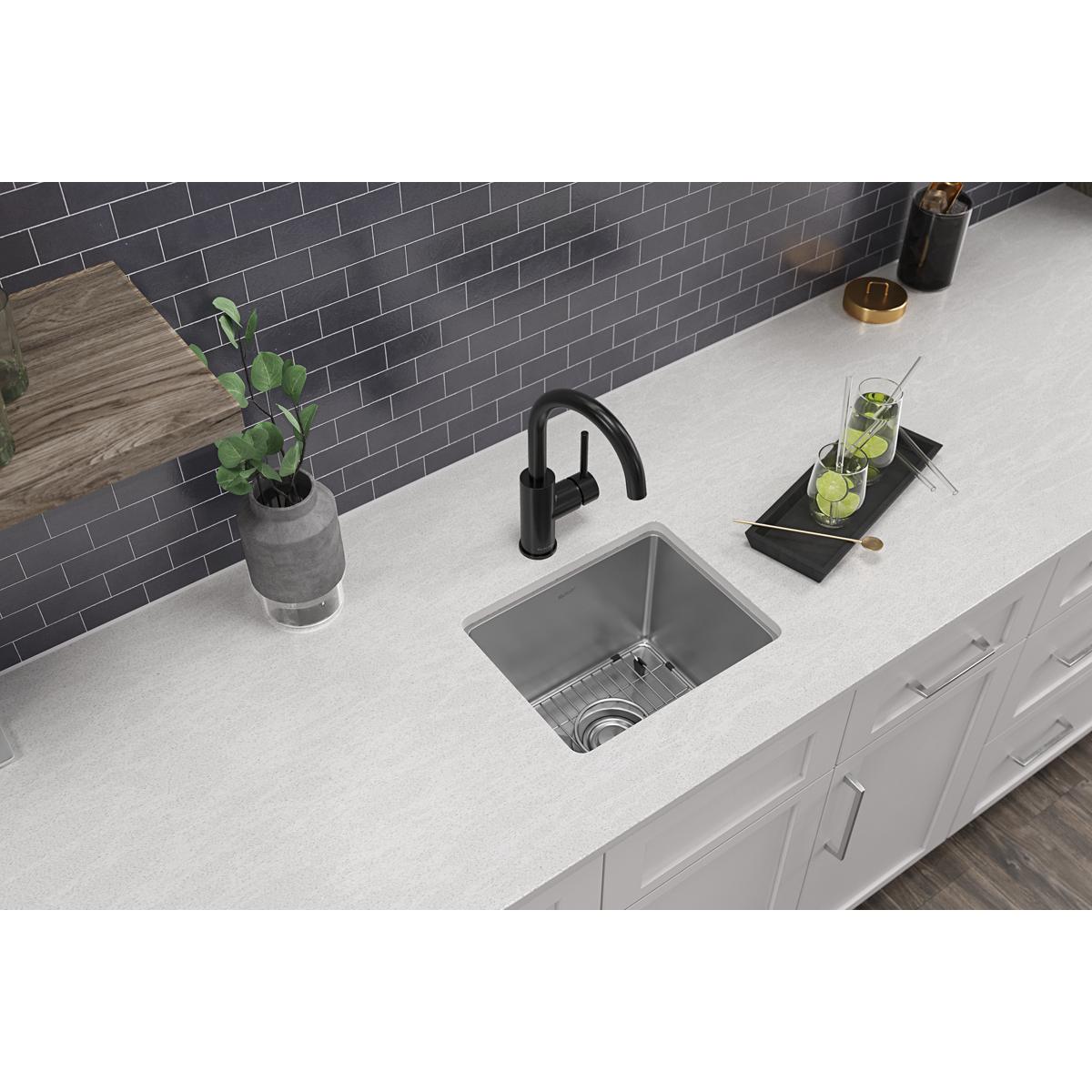 Stainless steel single bowl bar sink with one faucet hole installed in white countertop next to black faucet.