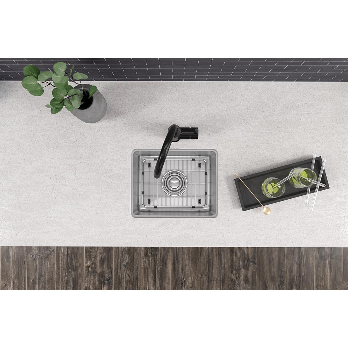 Stainless steel single bowl bar sink with drain grid and black faucet mounted in countertop.