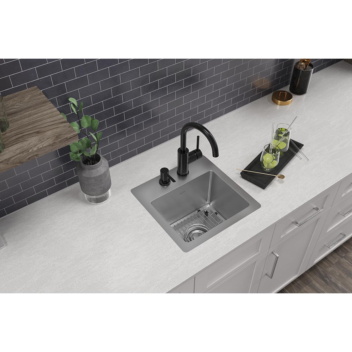 Stainless steel square bar sink with single bowl, two faucet holes, and drain grid installed in white countertop.