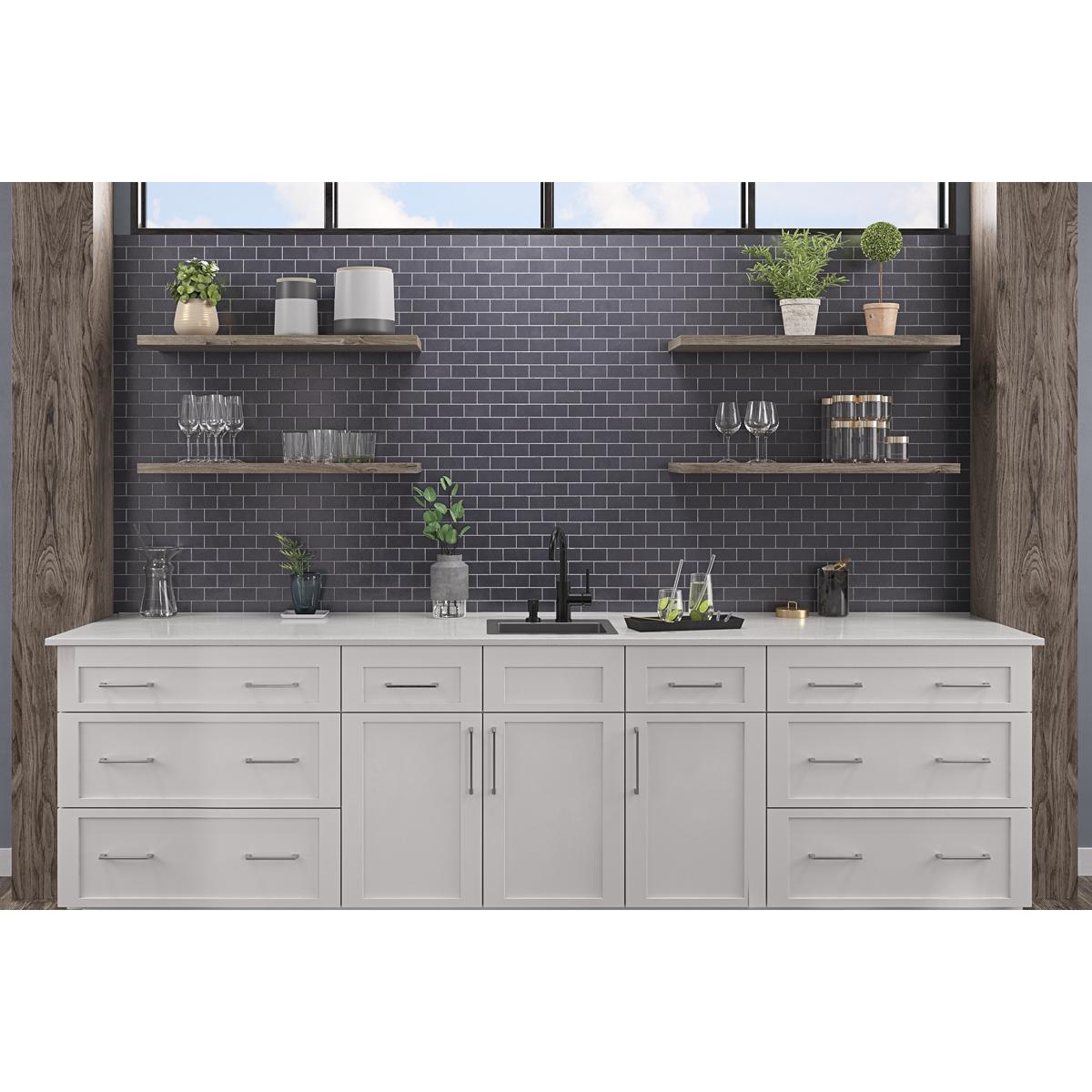 Stainless steel single bowl bar sink with two faucet holes mounted in white cabinetry with black faucet.