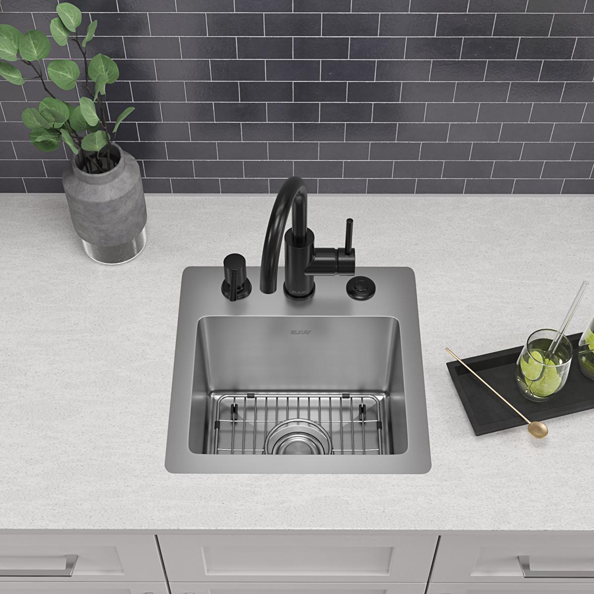 Stainless steel single bowl bar sink with black faucet, drain grid, and three mounting holes installed in white countertop.
