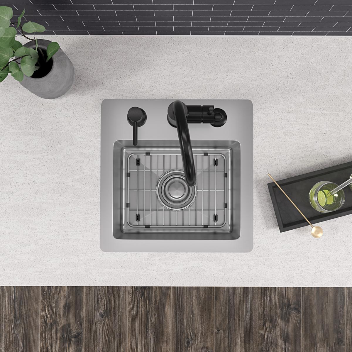 Stainless steel square bar sink with single bowl, grid insert, and black wall-mounted faucet with curved spout installed in c