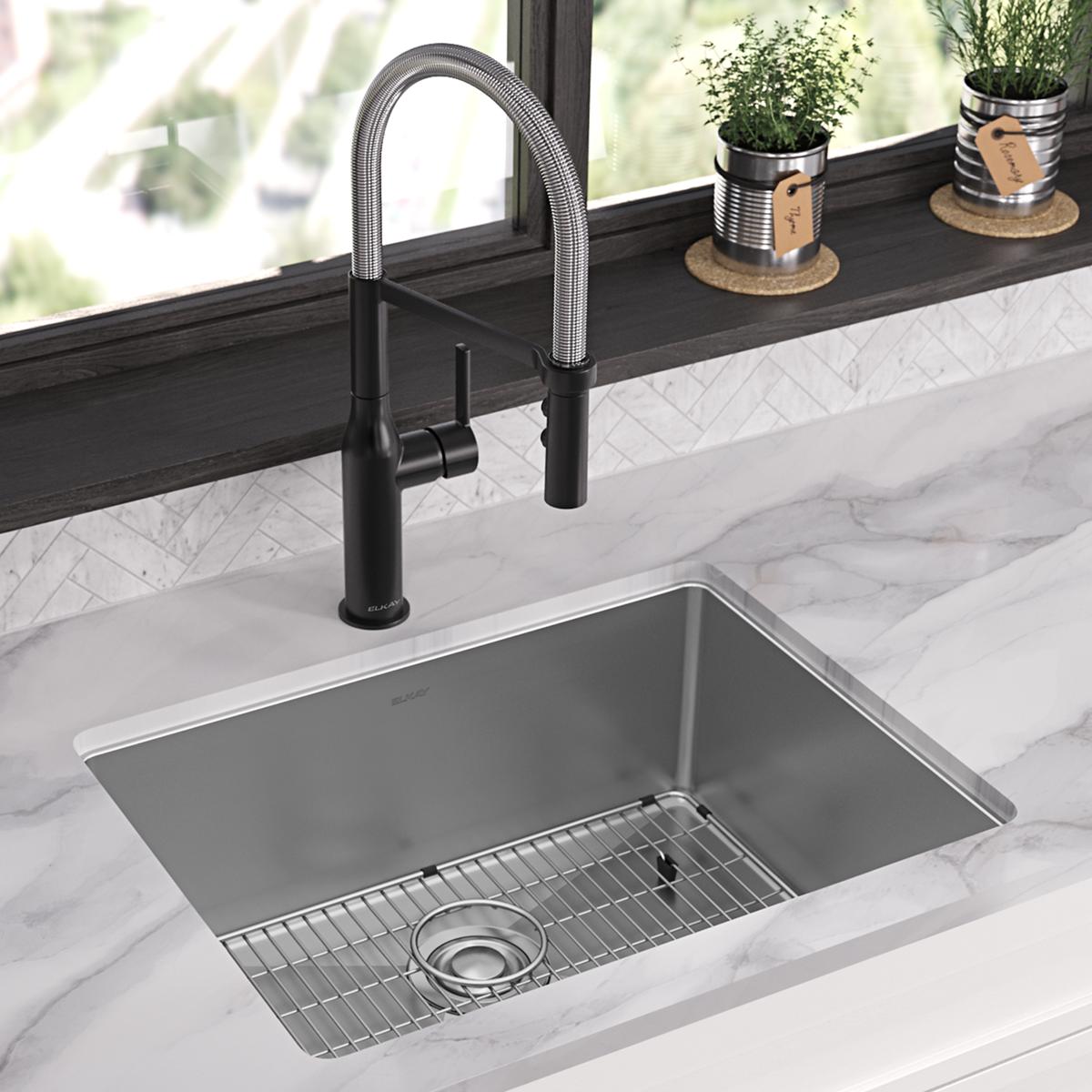 Stainless steel single bowl sink with drain grid and black pull-down faucet installed in marble countertop.