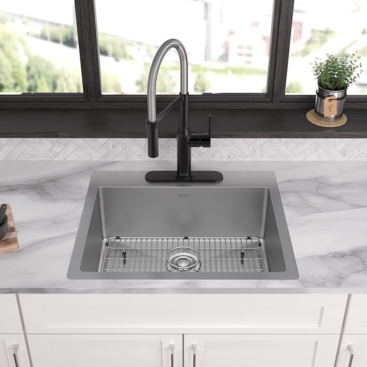 Stainless steel single bowl sink with drain grid and black pull-down faucet mounted on marble countertop.