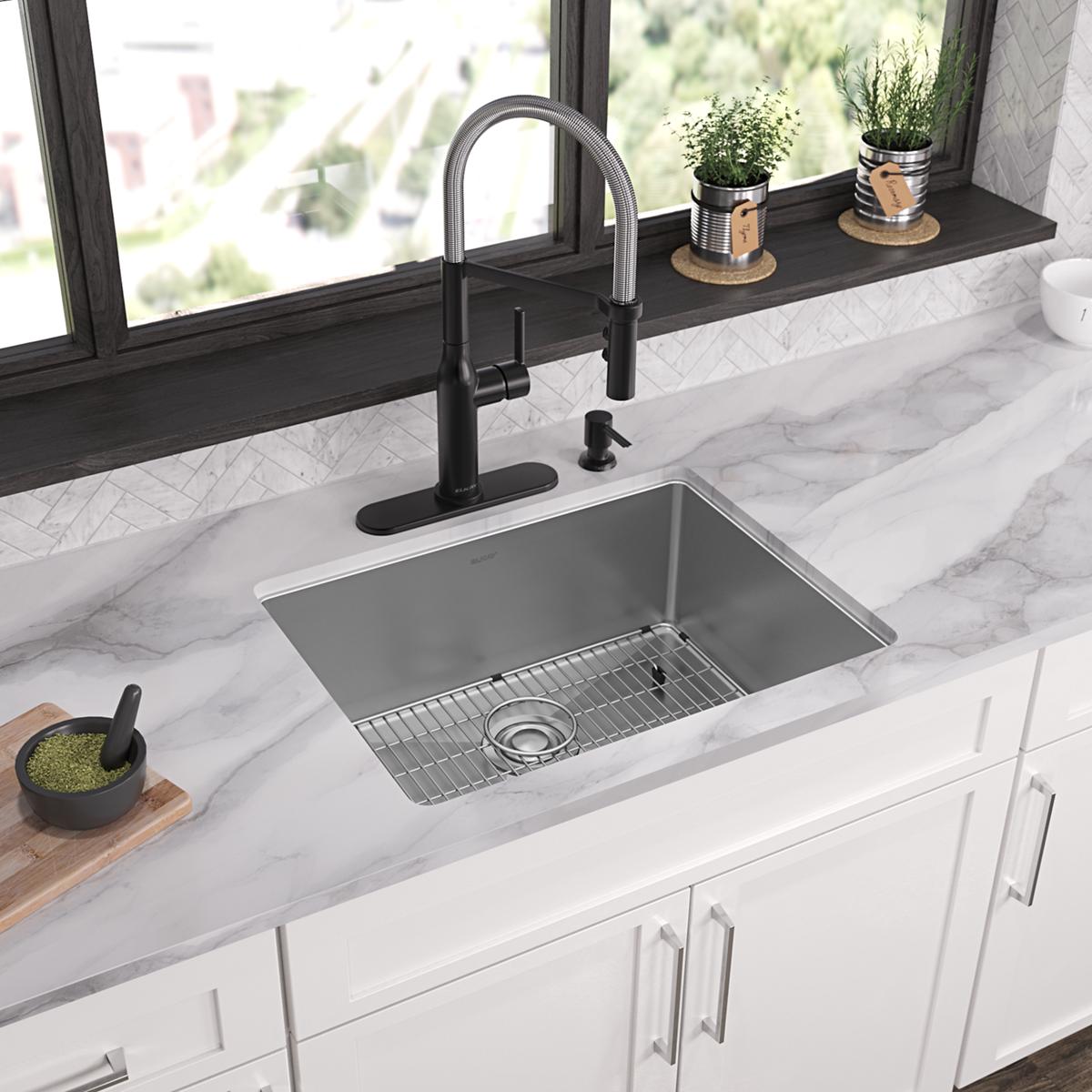 Stainless steel single bowl sink with four holes, wire grid, and black pull-down faucet installed in white countertop.
