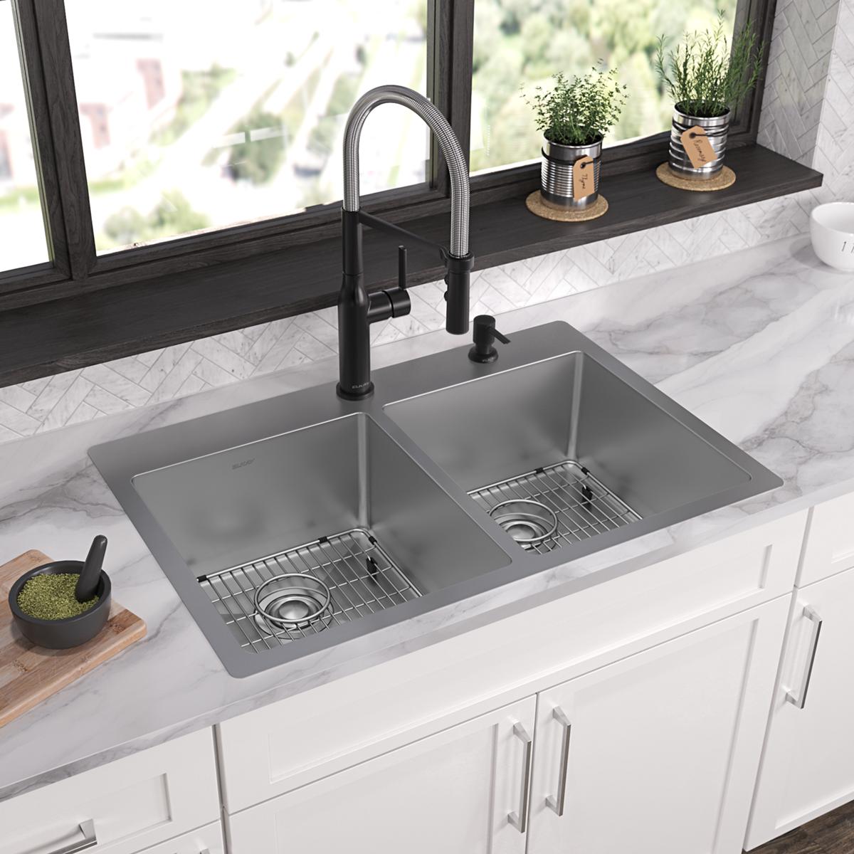 Stainless steel double bowl sink with two compartments, metal grid inserts, and black pull-down faucet installed in white cou