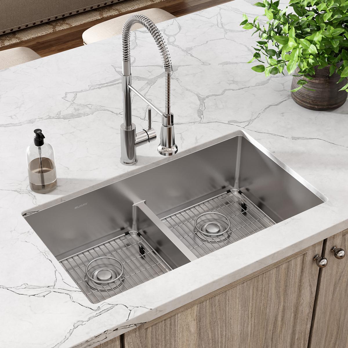 Stainless steel dual bowl sink with divider, grid inserts, and chrome pull-down faucet mounted in white marble countertop.