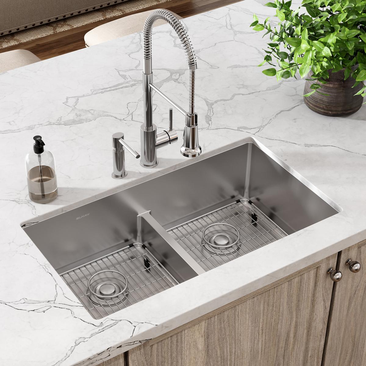 Stainless steel double bowl sink with divider installed in marble countertop, featuring pull-down faucet and two basin grids.