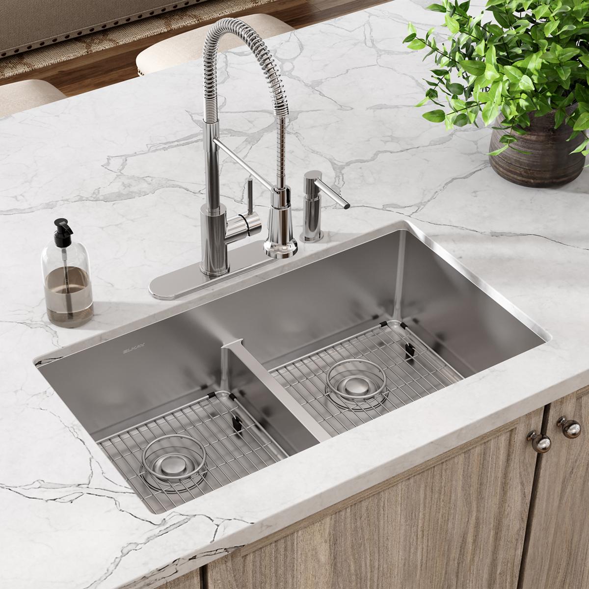 Stainless steel double bowl sink with unequal basins, grid inserts, and chrome pull-down faucet mounted on marble countertop.