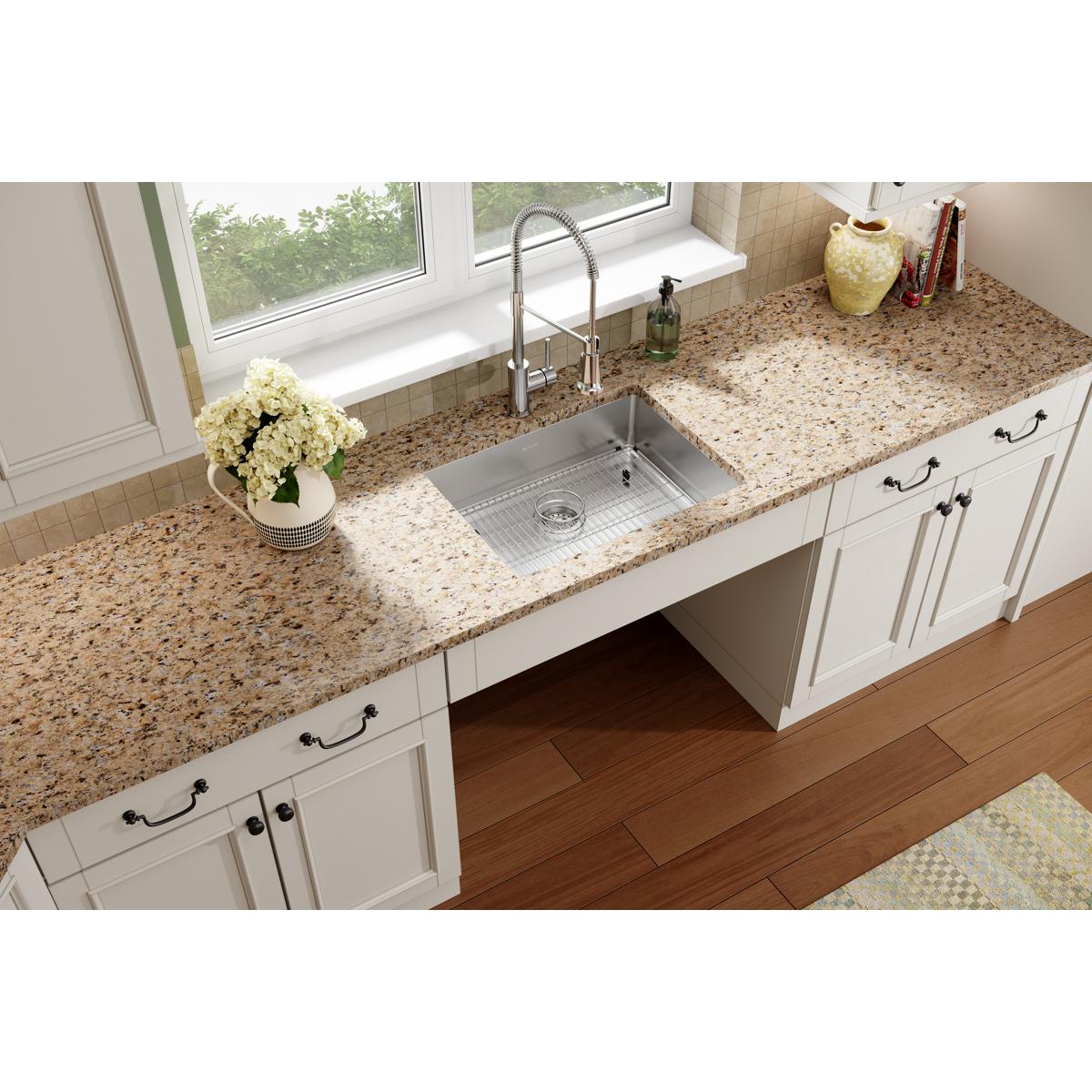 Stainless steel single bowl sink installed in granite countertop with chrome faucet and white cabinetry in kitchen.