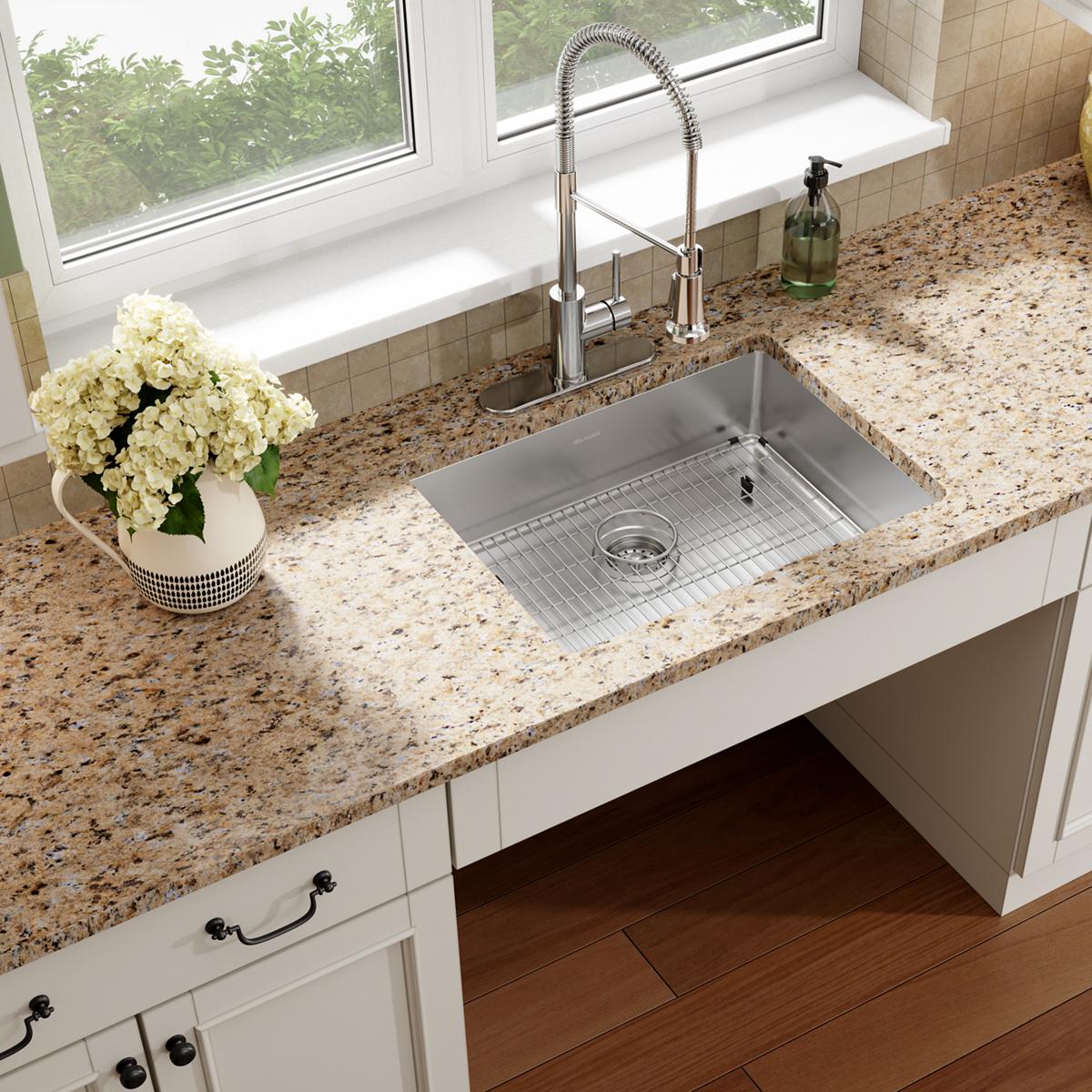 Stainless steel single bowl sink with grid and sprayer faucet installed in granite countertop with white cabinetry.