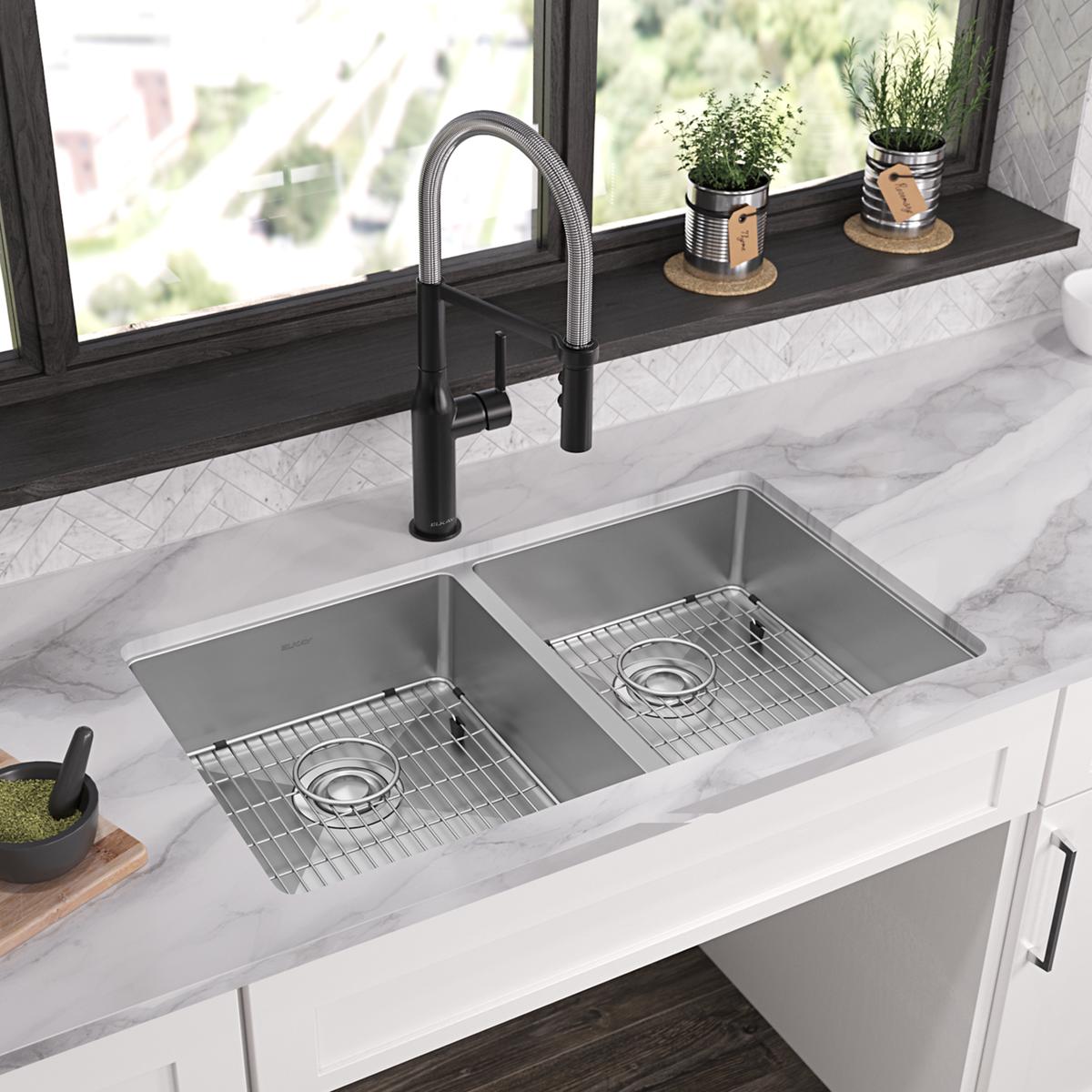 Stainless steel double bowl sink with equal-sized compartments, grid inserts, and black pull-down faucet mounted on marble co