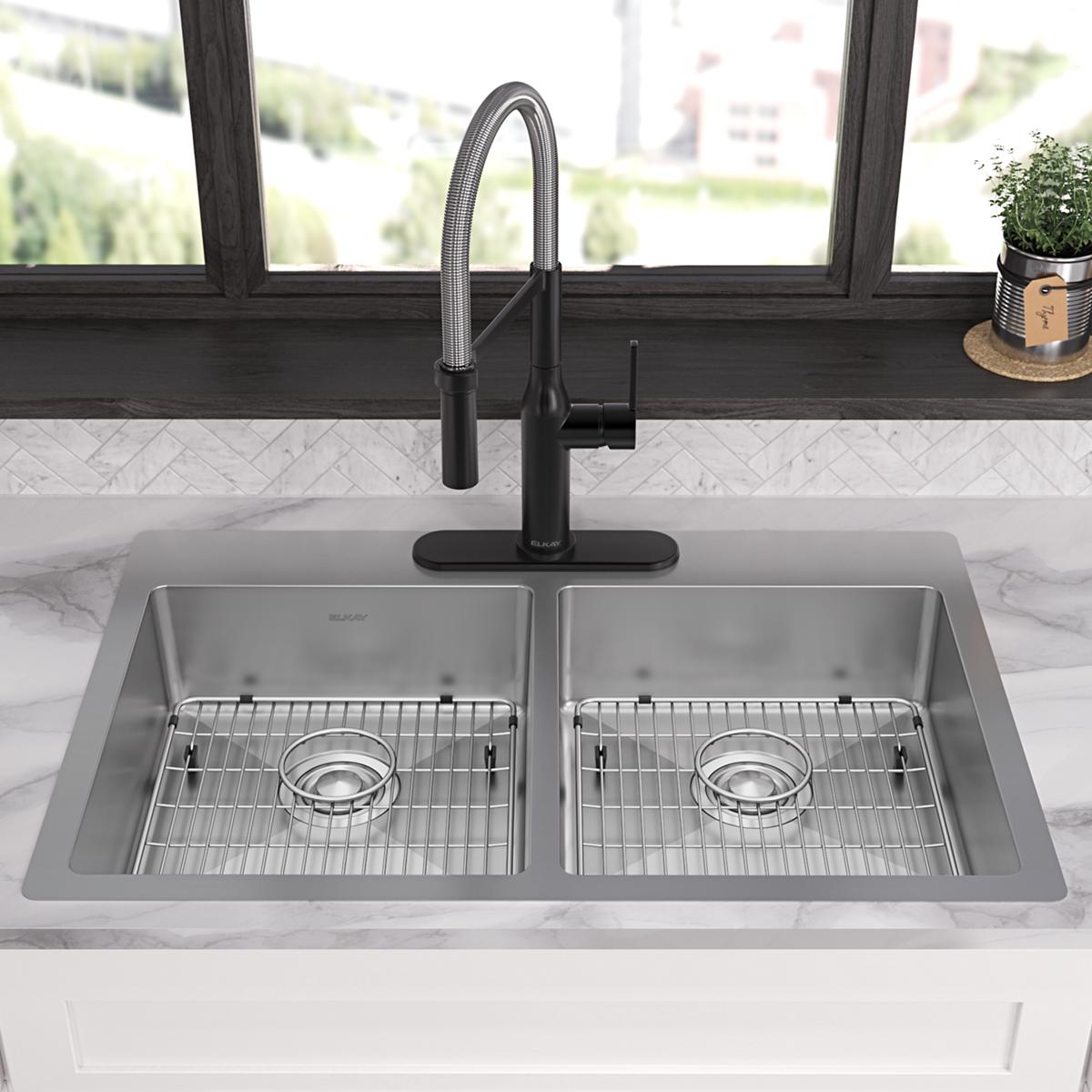 Stainless steel double bowl sink with two wire grid inserts and black pull-down faucet mounted on marble countertop.