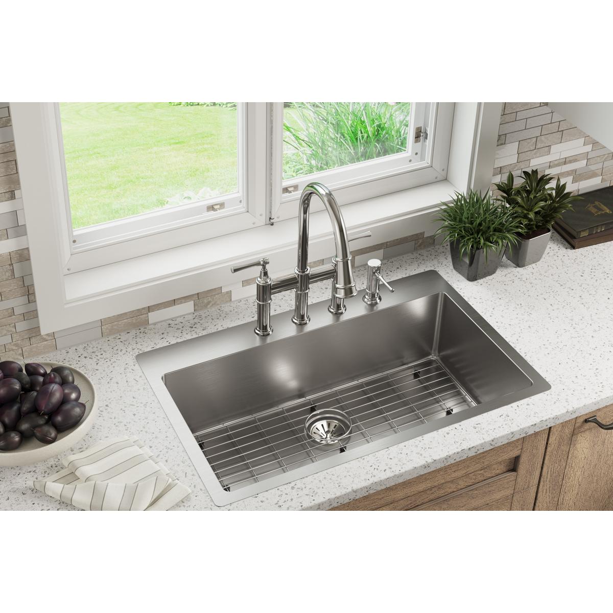 Stainless steel single bowl kitchen sink with two faucet holes, chrome faucet, and grid insert installed in white countertop.