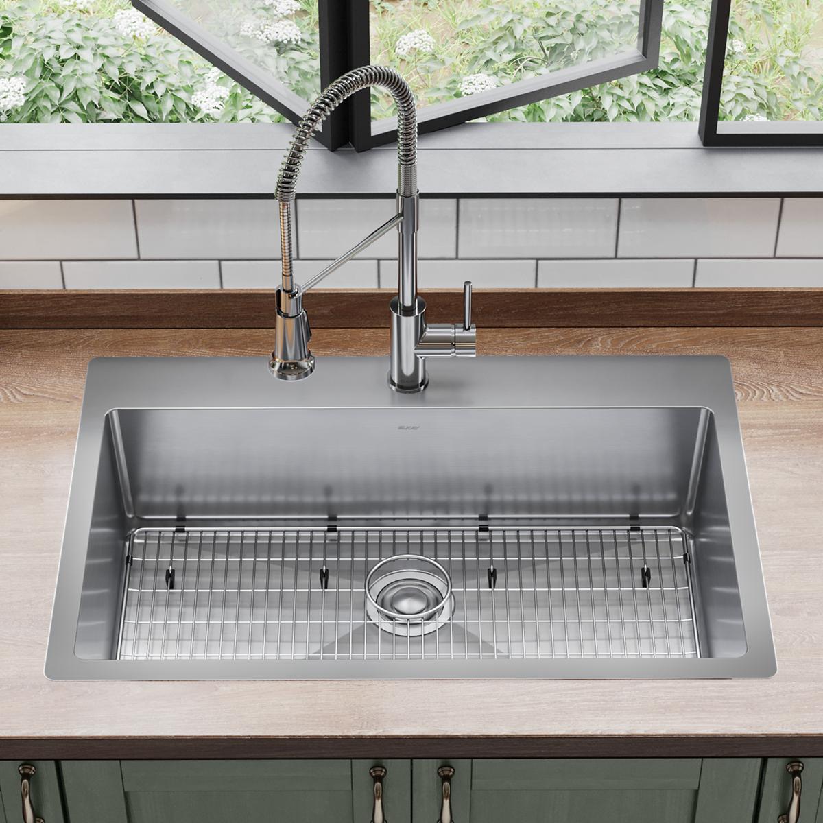 Stainless steel single bowl sink with sprayer faucet and grid strainer installed in countertop.