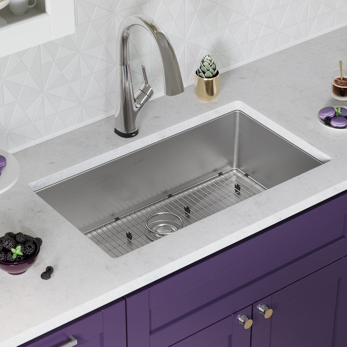 Stainless steel rectangular single bowl sink mounted in white countertop with chrome pull-down faucet and grid rack.