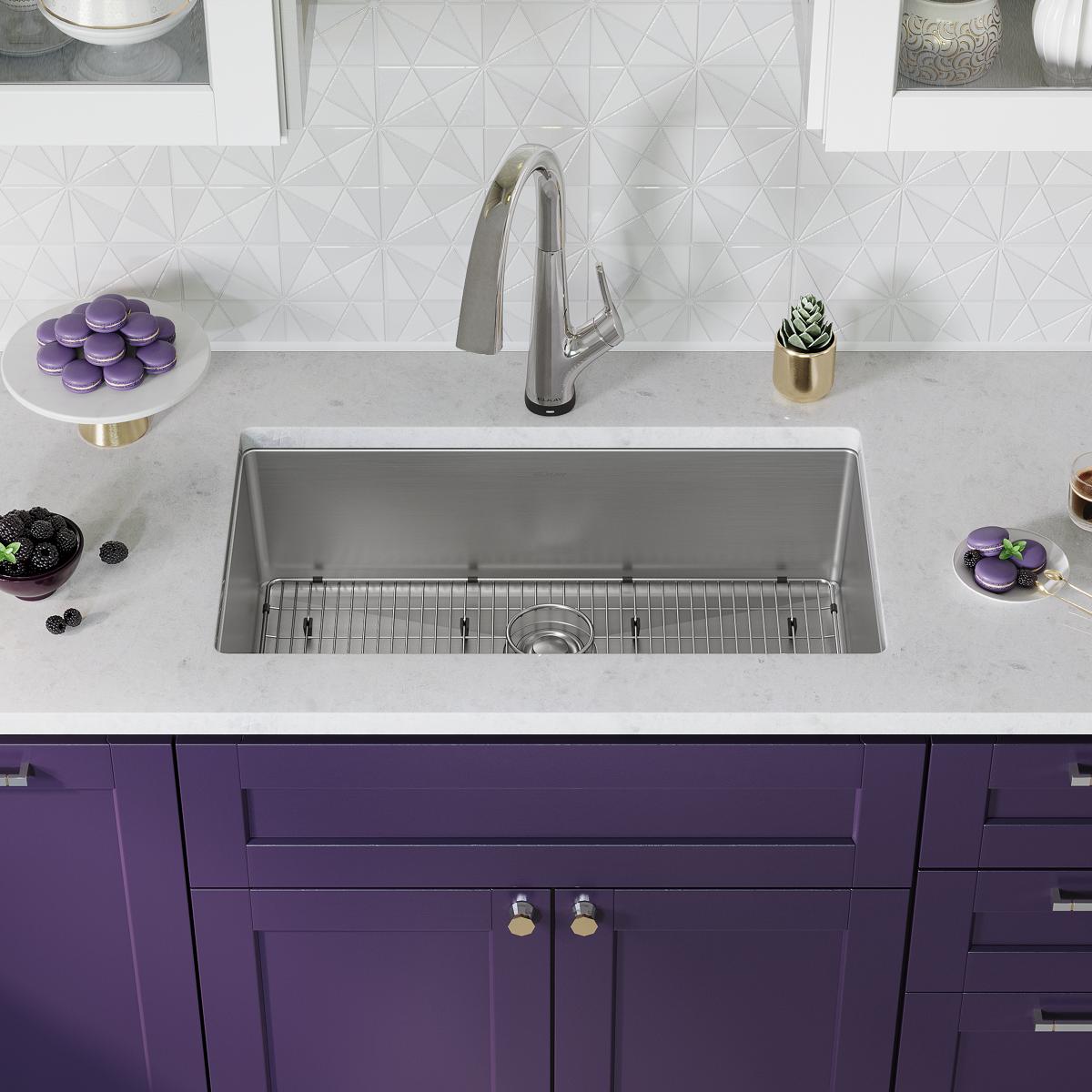 Stainless steel rectangular sink with single bowl, grid strainer, and chrome pull-down faucet installed in white countertop a