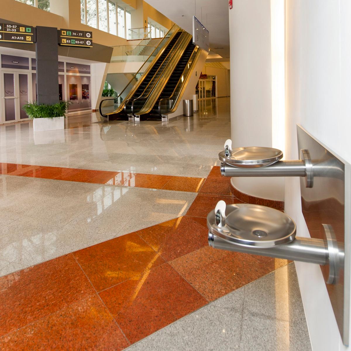 Two stainless steel wall-mounted drinking fountains with round bowls installed in a public building corridor.
