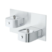 Stainless steel bi-level water fountain with two drinking bowls mounted on white backplate, each with chrome spout and contro