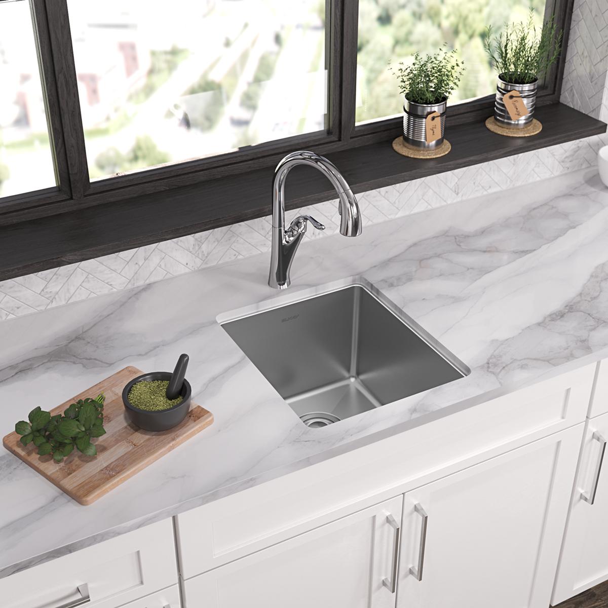 Stainless steel undermount sink with single rounded bowl installed in white marble countertop with chrome faucet.