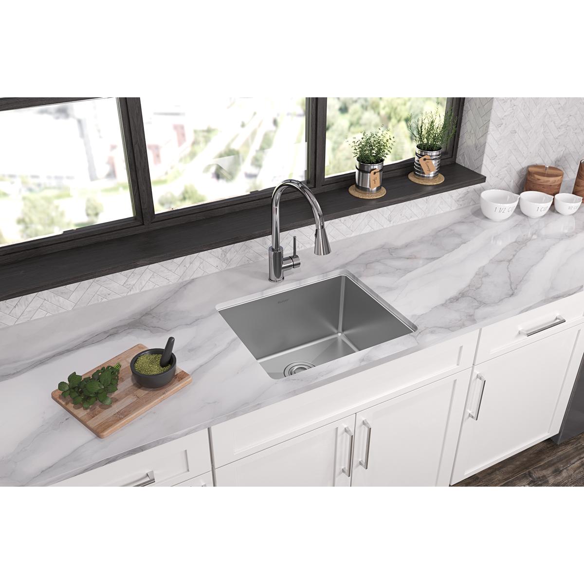 Stainless steel single bowl undermount sink installed in white marble countertop with chrome faucet.