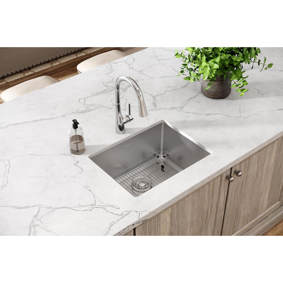 Stainless steel undermount sink with rounded corners installed in white marble countertop, includes metal grid insert.