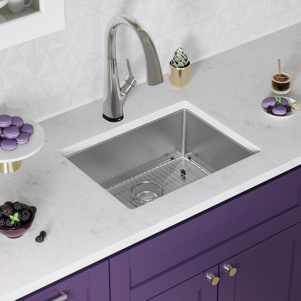 Stainless steel single bowl undermount sink with pull-down faucet and drain grid installed in white countertop above purple c