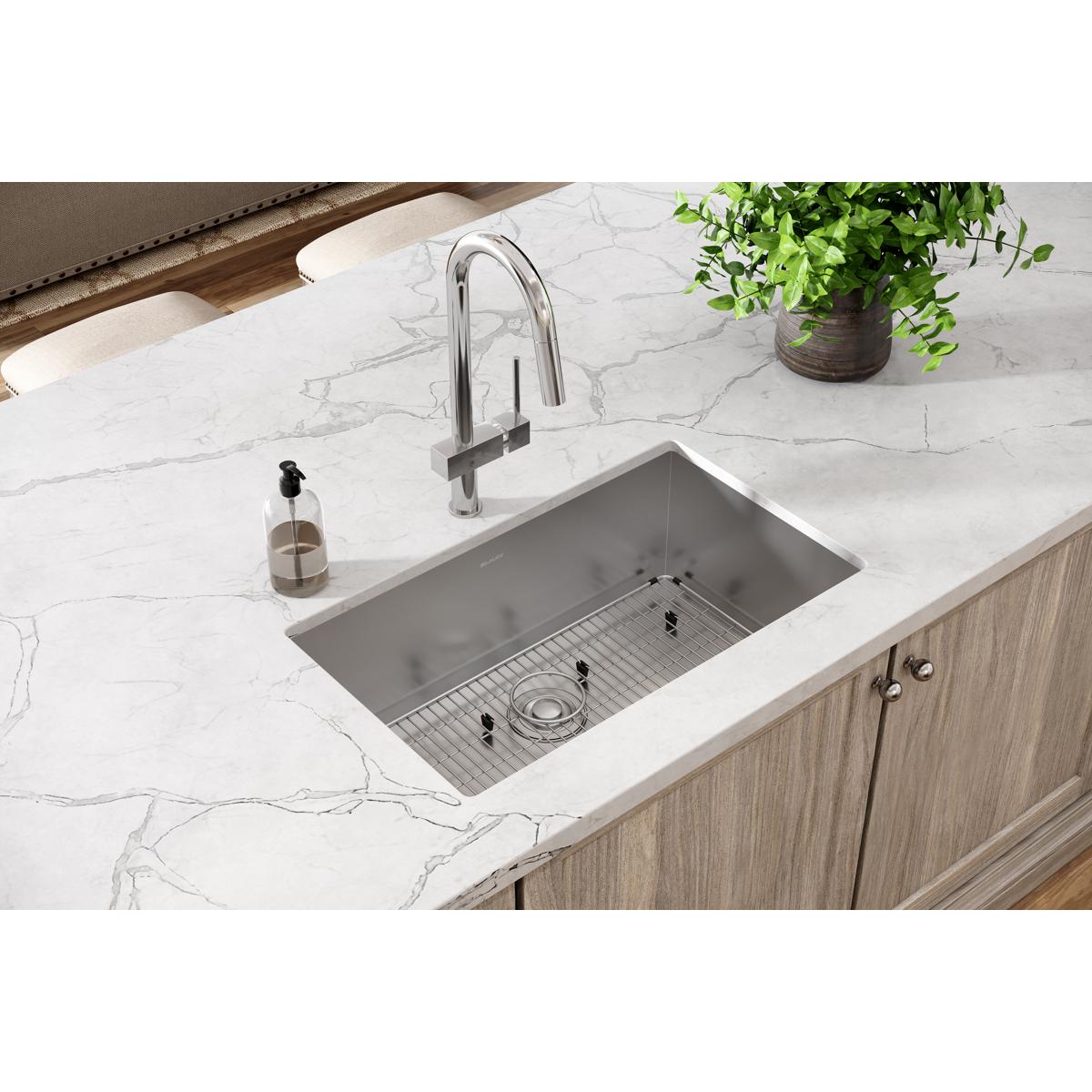 Stainless steel undermount sink with rounded bowl, drain grid, and faucet installed in white marble countertop.