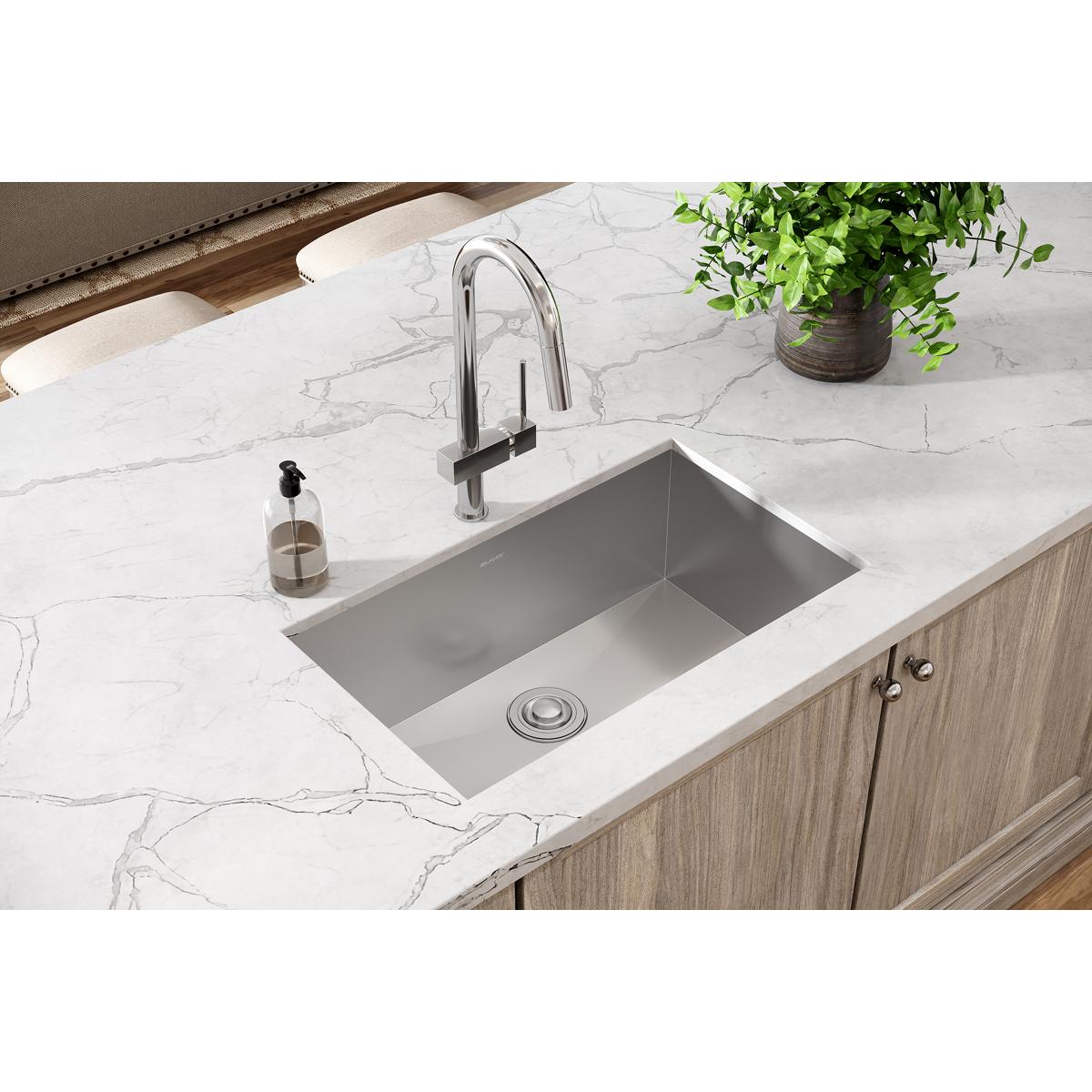 Stainless steel undermount sink with rounded single bowl installed in white marble countertop with chrome faucet.