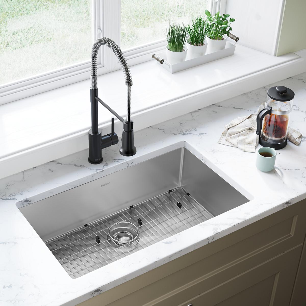 Stainless steel undermount kitchen sink with single bowl, grid insert, and black pull-down faucet installed in marble counter