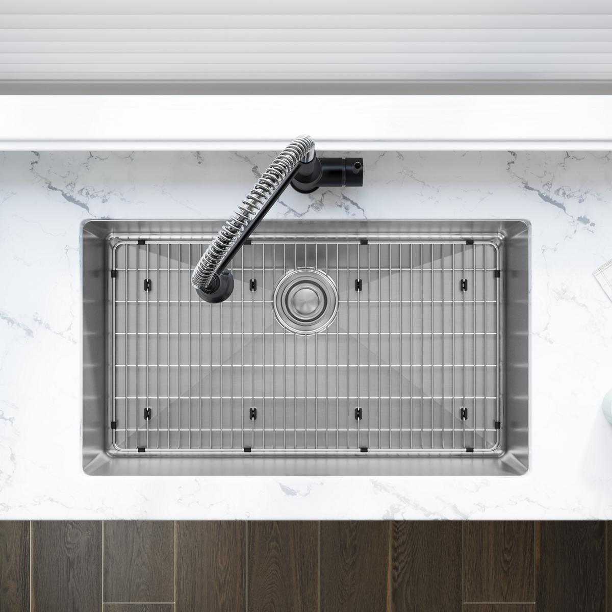 Stainless steel single bowl undermount sink with grid and drain strainer, installed below marble countertop with chrome fauce