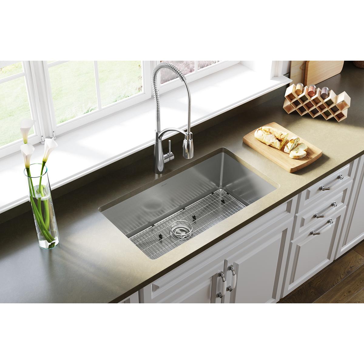 Stainless steel undermount sink with single bowl, drain grid, and chrome pull-down faucet installed in countertop.