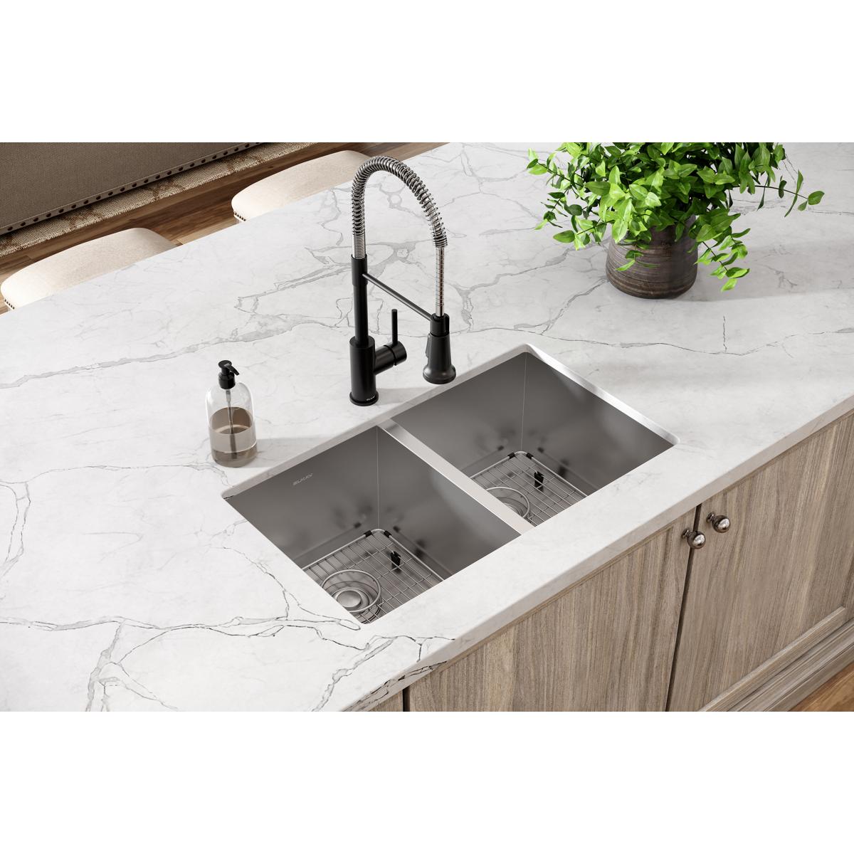 Stainless steel double bowl undermount sink with rounded corners installed in white marble countertop, paired with black fauc