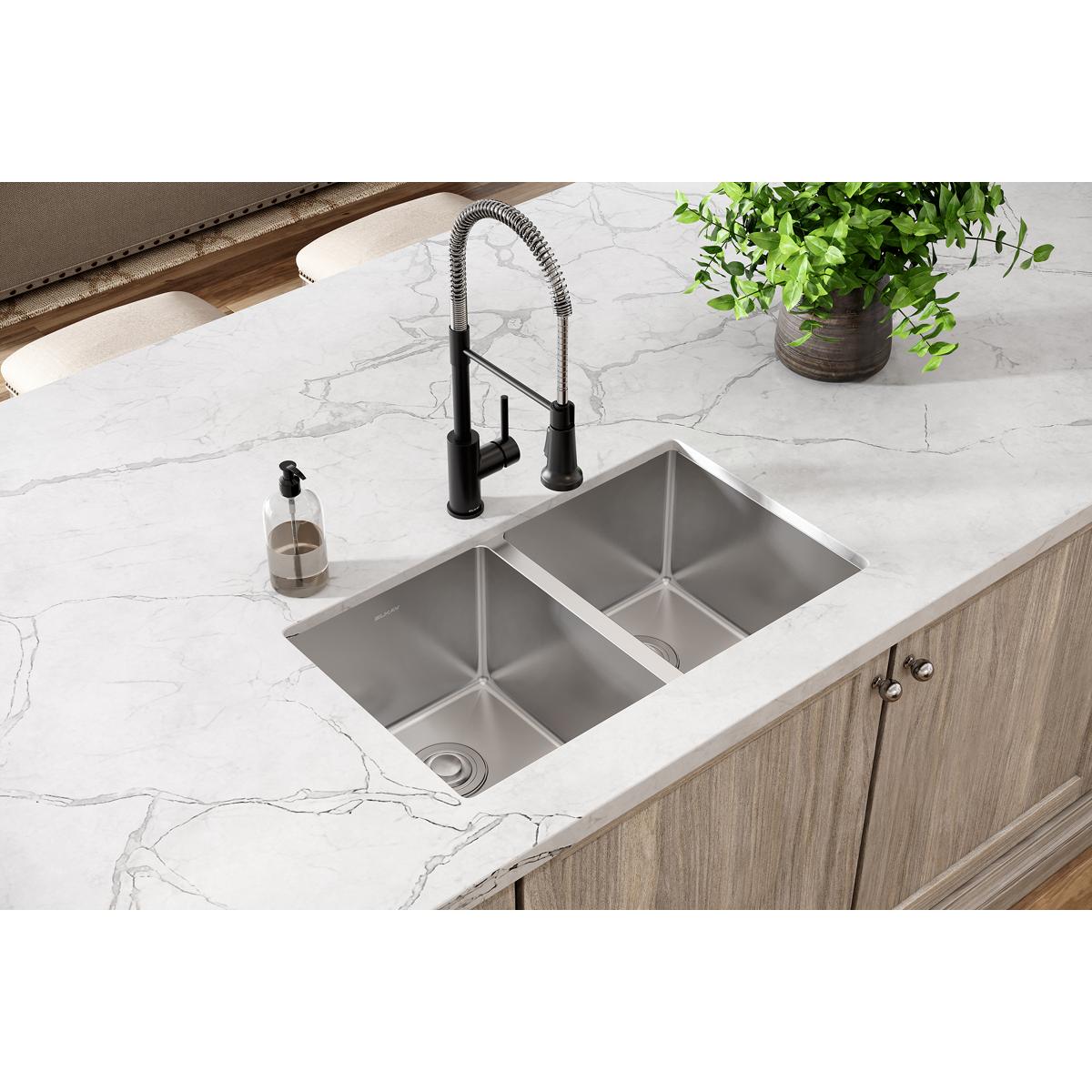Stainless steel double bowl undermount sink with rounded corners installed in white marble countertop with black faucet.