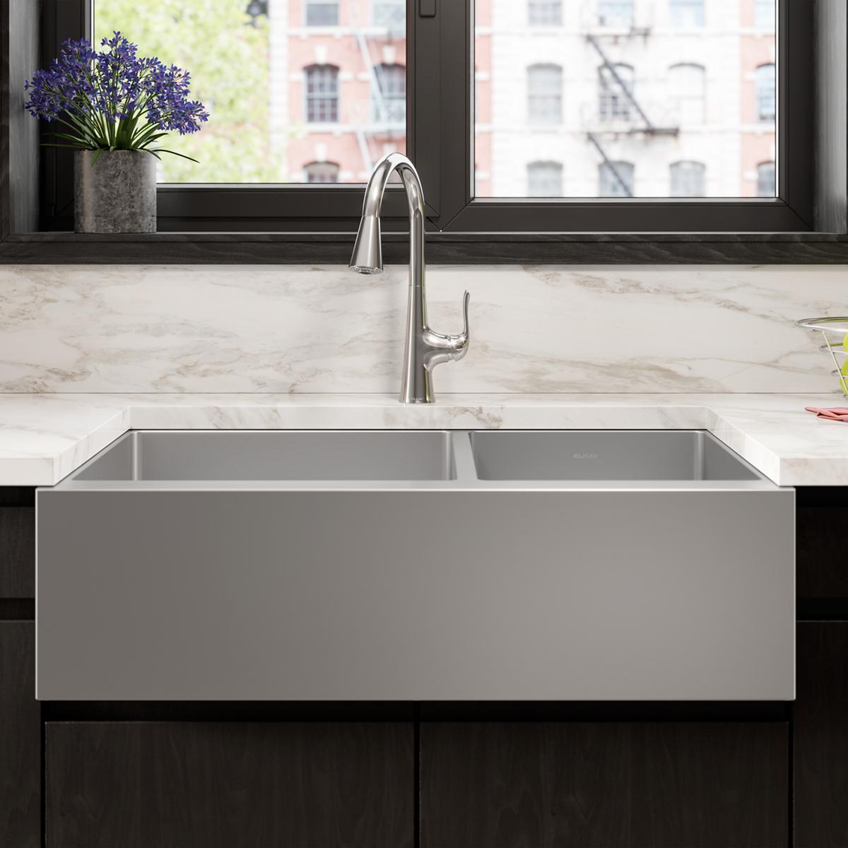 Stainless steel double bowl farmhouse sink with tall faucet installed in marble countertop.