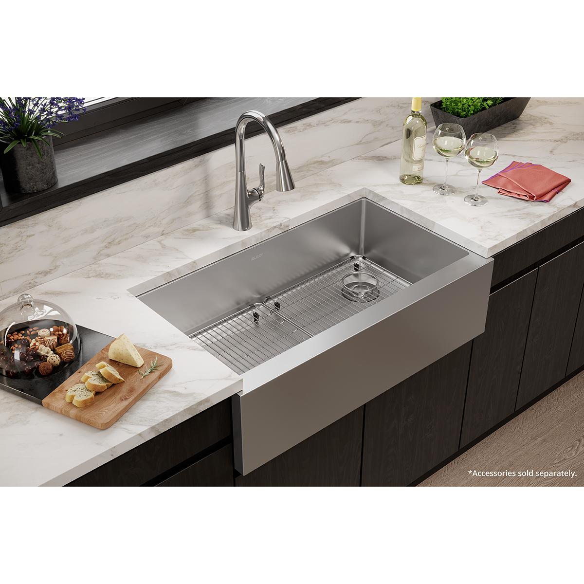 Stainless steel single bowl farmhouse sink with tall front apron installed in marble countertop with faucet.