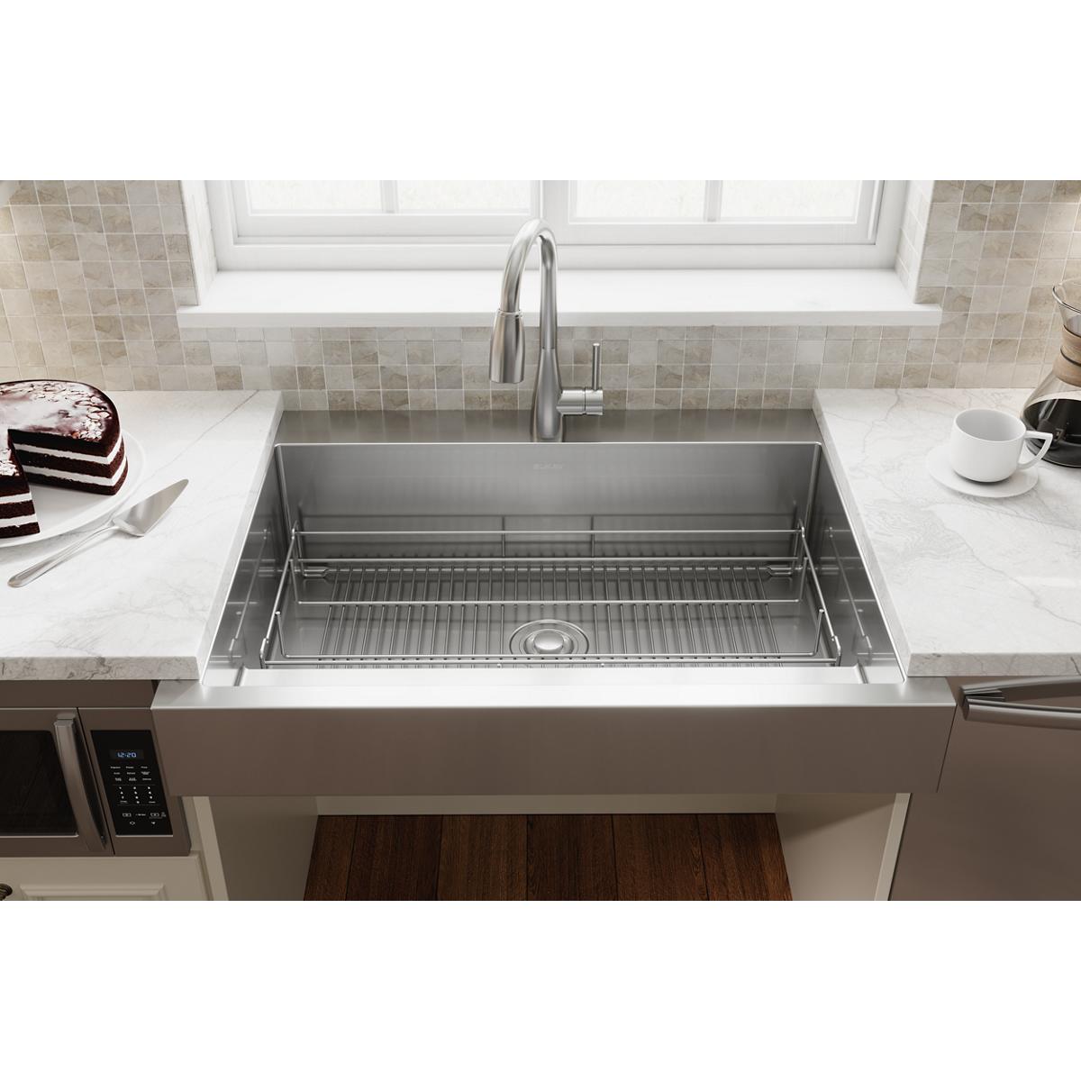 Stainless steel sink grid with parallel ridges positioned in bottom of farmhouse kitchen sink basin.