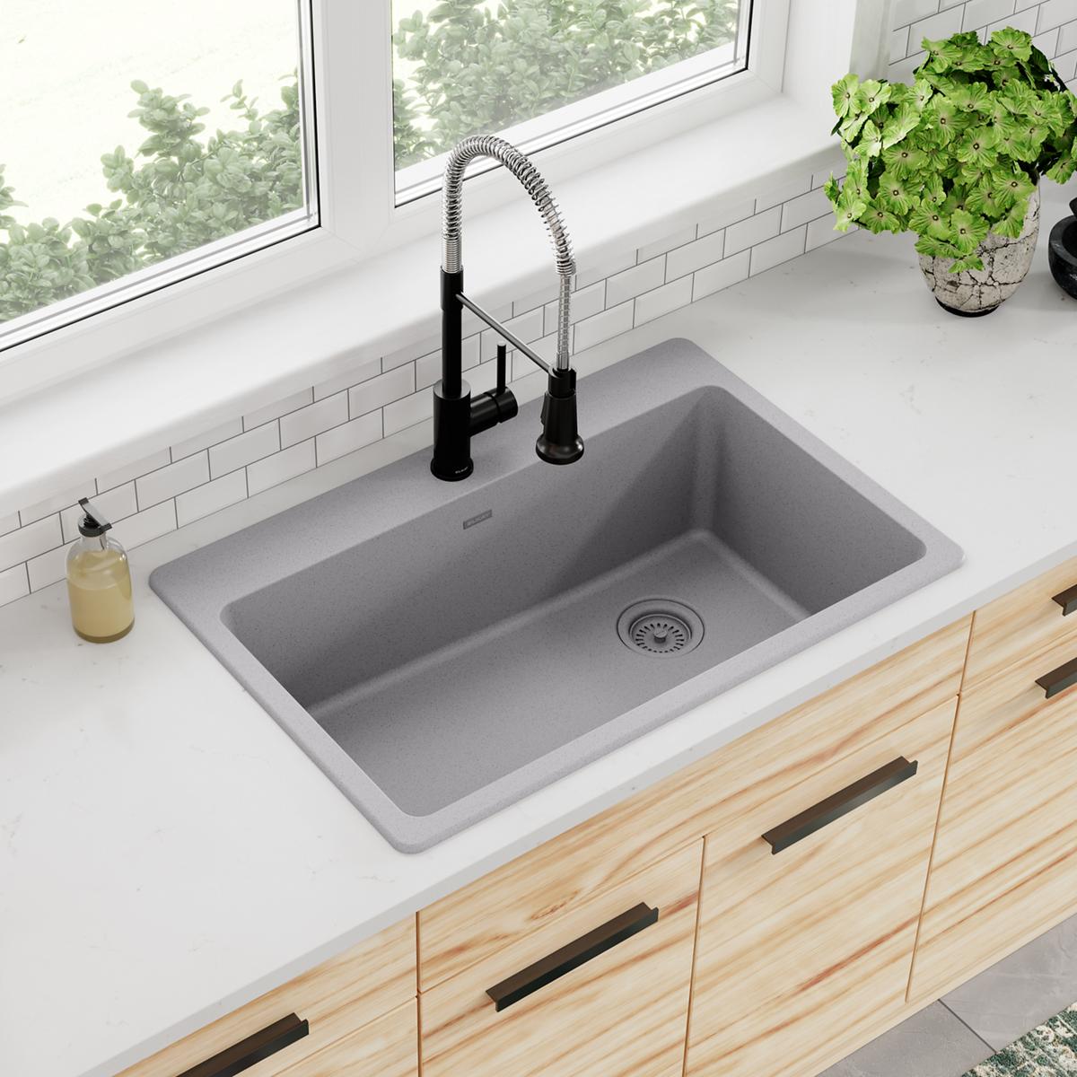 Greystone quartz drop-in sink with single bowl and black pull-down faucet installed in white countertop.