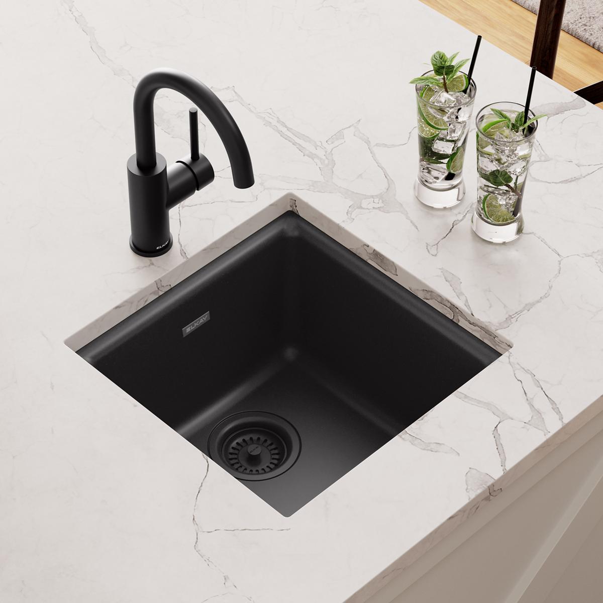 Black quartz single bowl bar sink installed in white countertop with black faucet and drain strainer.