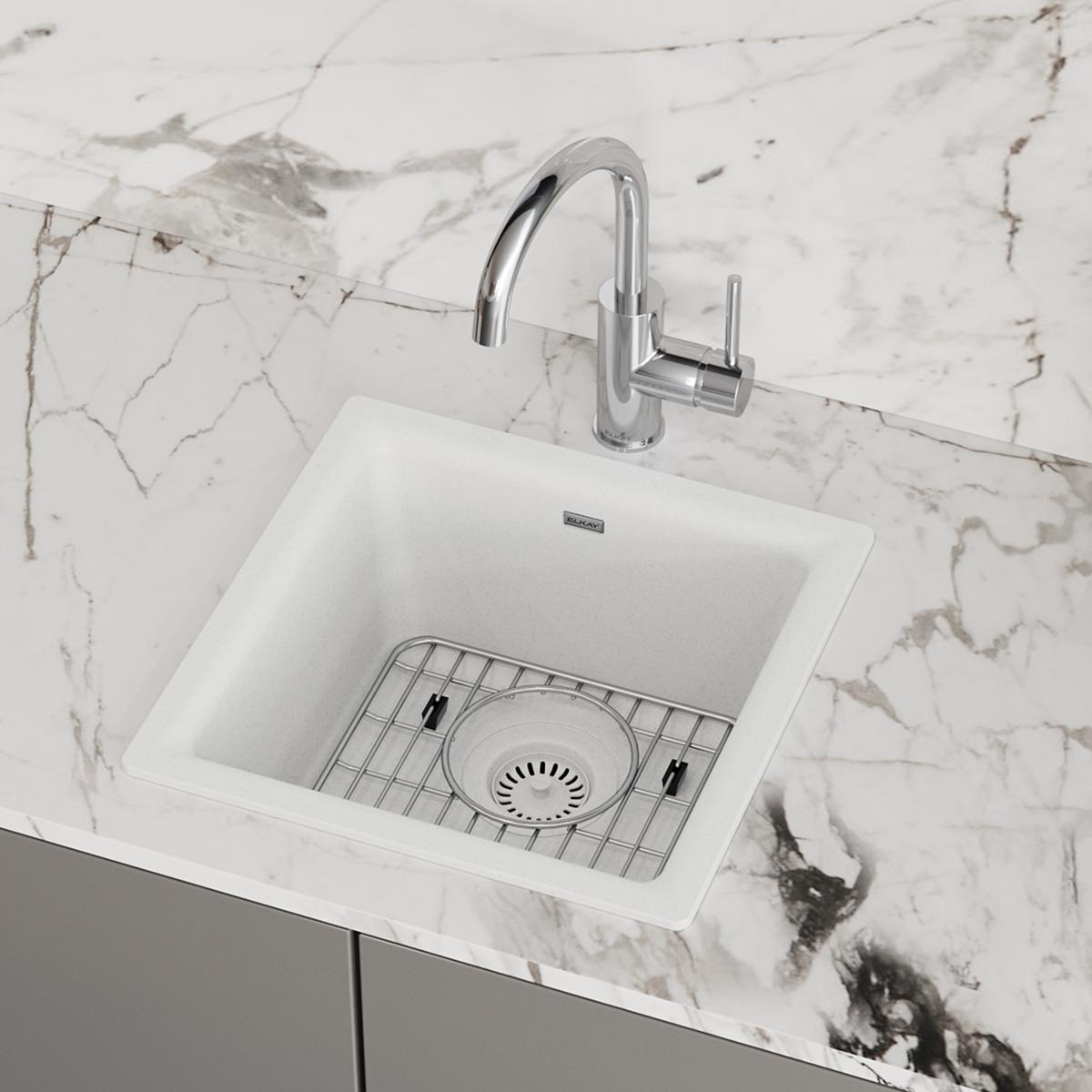 White quartz square bar sink with single bowl, chrome faucet, and wire grid strainer on marble countertop.