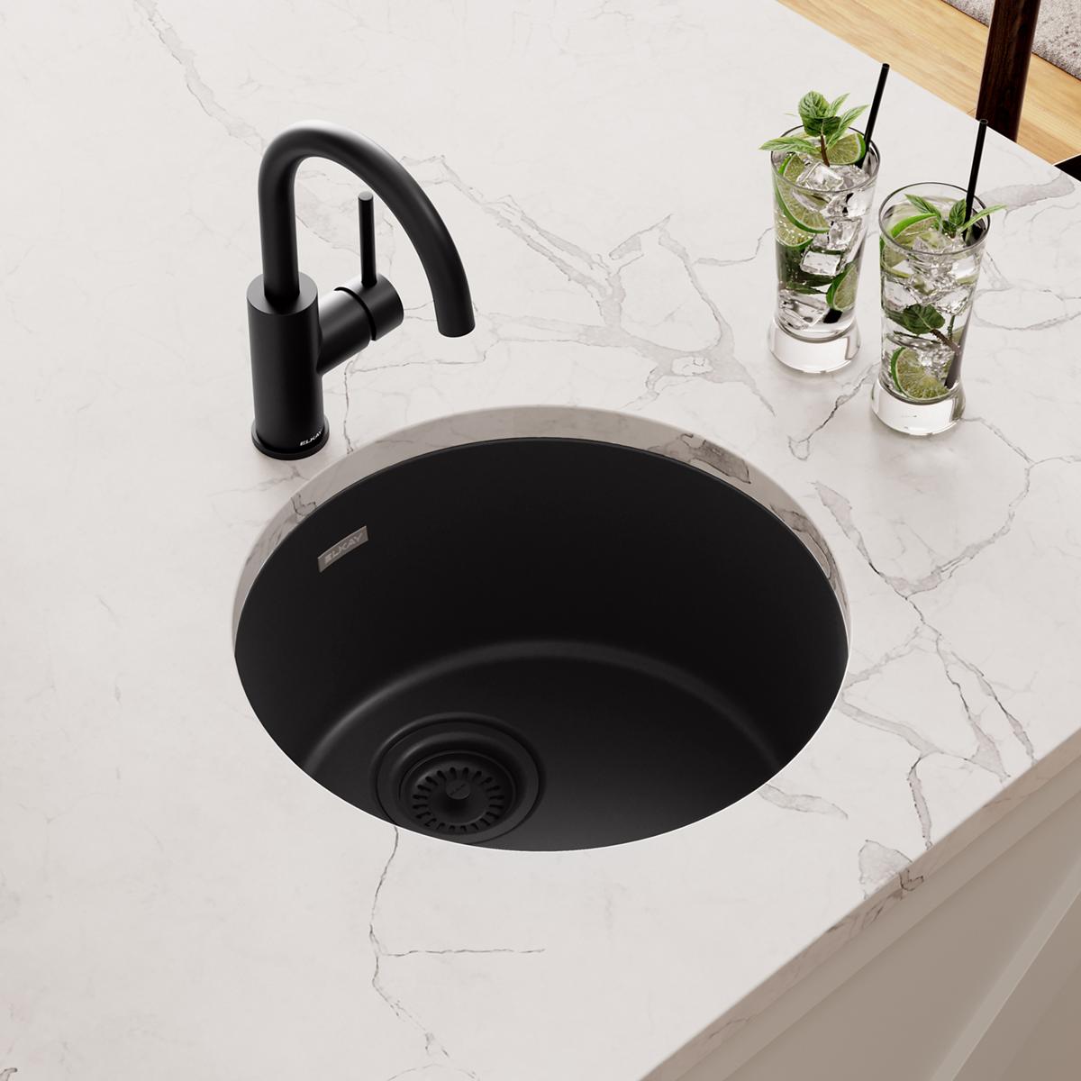 Black quartz round bar sink with matching black faucet installed in white countertop.