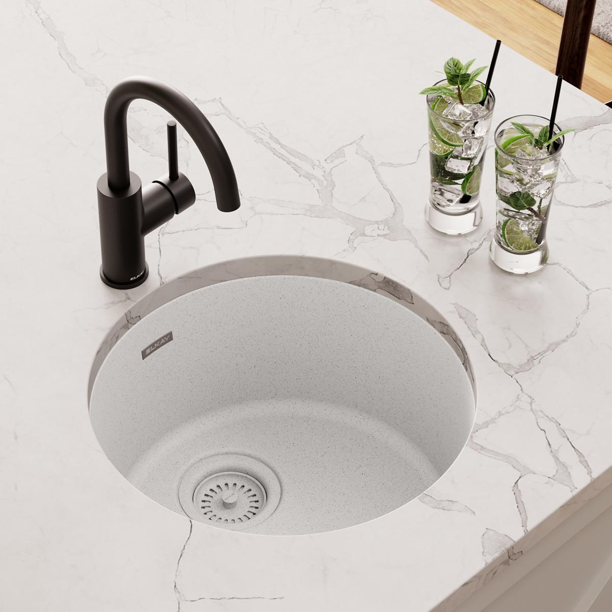 White quartz round single bowl bar sink with black faucet on marble countertop.