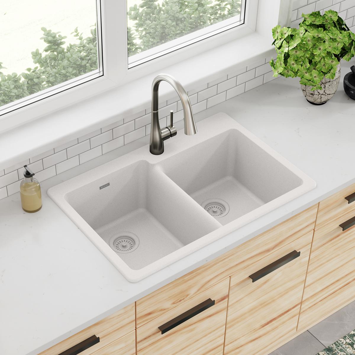 White quartz double bowl drop-in sink with offset basins and stainless steel faucet installed in countertop.