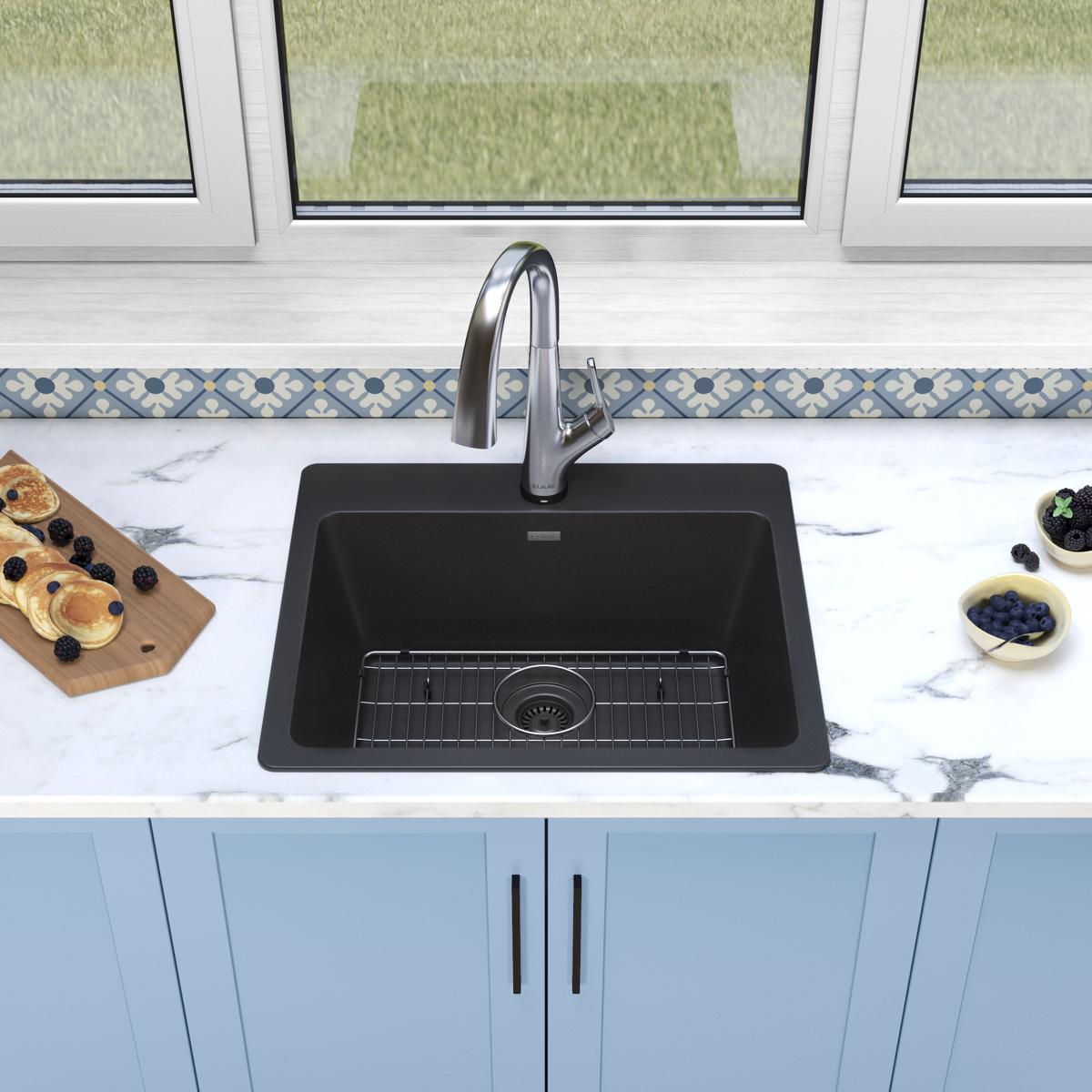 Black quartz drop-in sink with single bowl, metal arc faucet, and grid strainer in marble countertop kitchen.