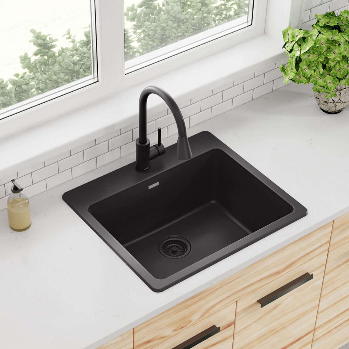 Black quartz drop-in kitchen sink with single bowl, drain, and black pull-down faucet installed in white countertop.