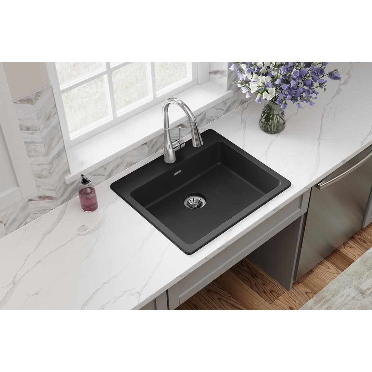 Black quartz single bowl drop-in sink with chrome faucet installed in white marble countertop.
