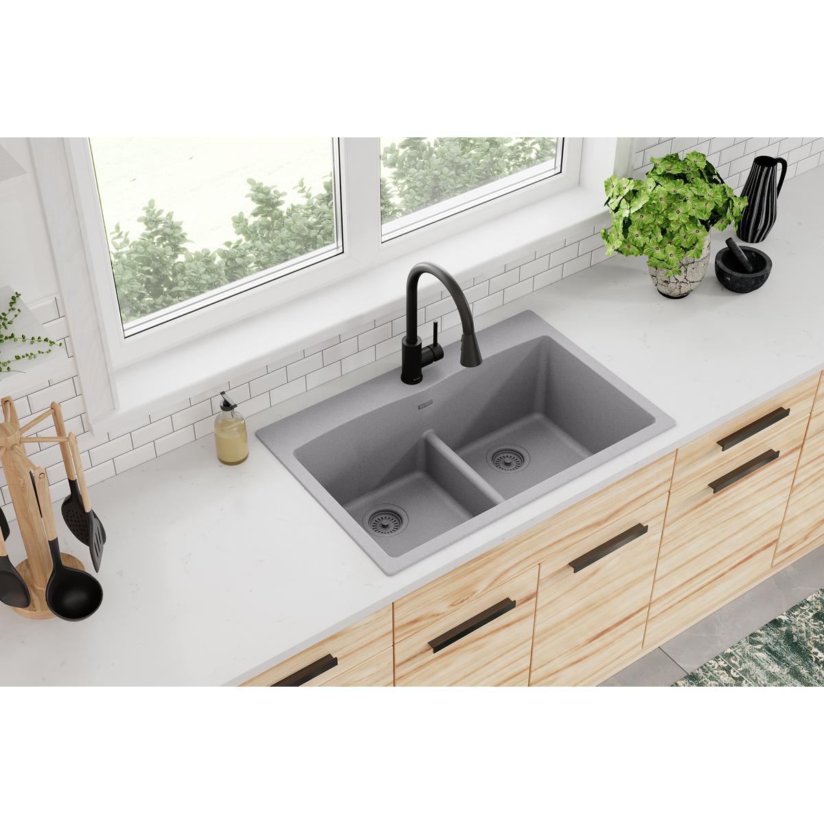 Greystone quartz drop-in sink with two equal bowls and center divider installed in light wood cabinetry with black faucet.