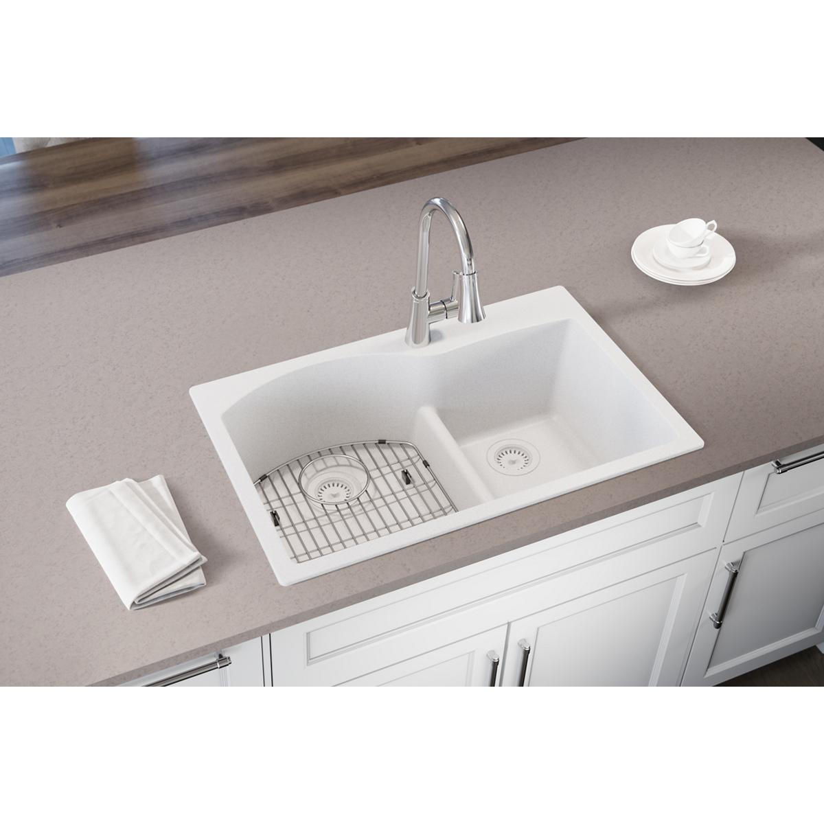 White quartz drop-in sink with two unequal bowls, divider, grid insert, and chrome faucet installed in countertop.