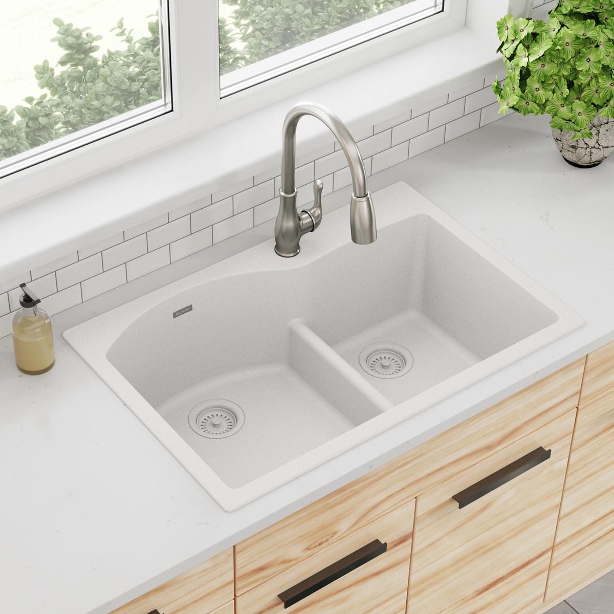 White quartz double bowl drop-in sink with offset basins, drains, and stainless steel faucet installed in countertop.