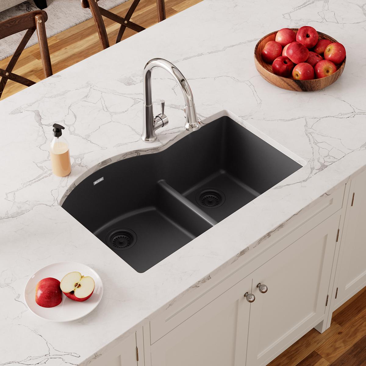Black quartz double bowl undermount sink with divider and chrome faucet installed in white marble countertop.